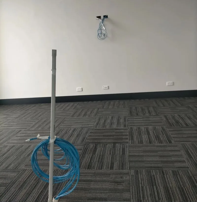 Empty boardroom with a cable draw pole and a coil of blue Cat6 on the floor, and Cat6 hanging from the wall where the display mounts