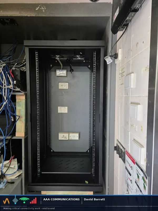 Full view of the new data cabinet with kept power outlets on the back panel, each carrying old handwritten labels, beside the existing equipment shelves.