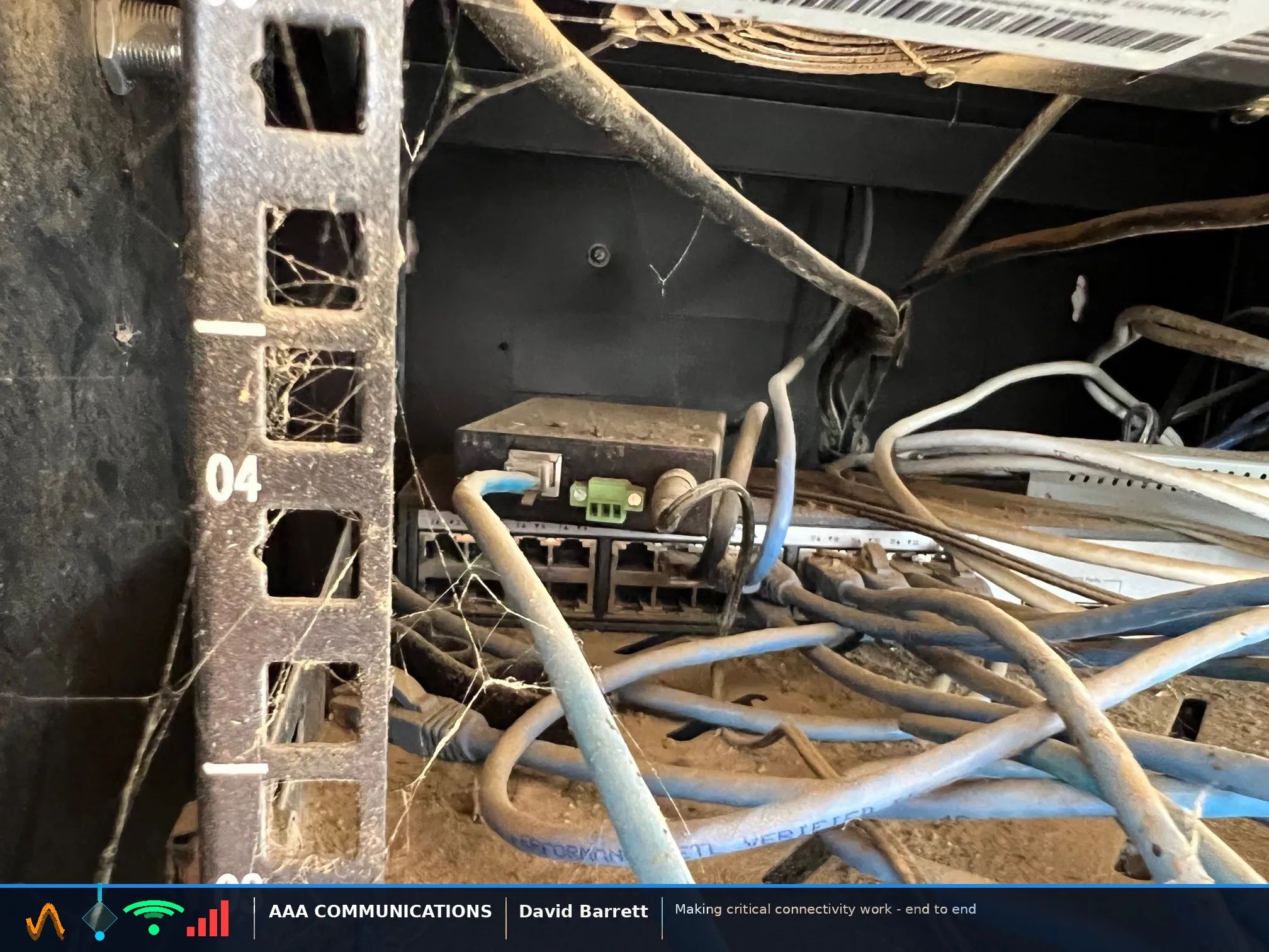 Network rack with cobwebs across the rail, dust on every switch port and a loose device sitting on top of the switch with no mounting or labelling